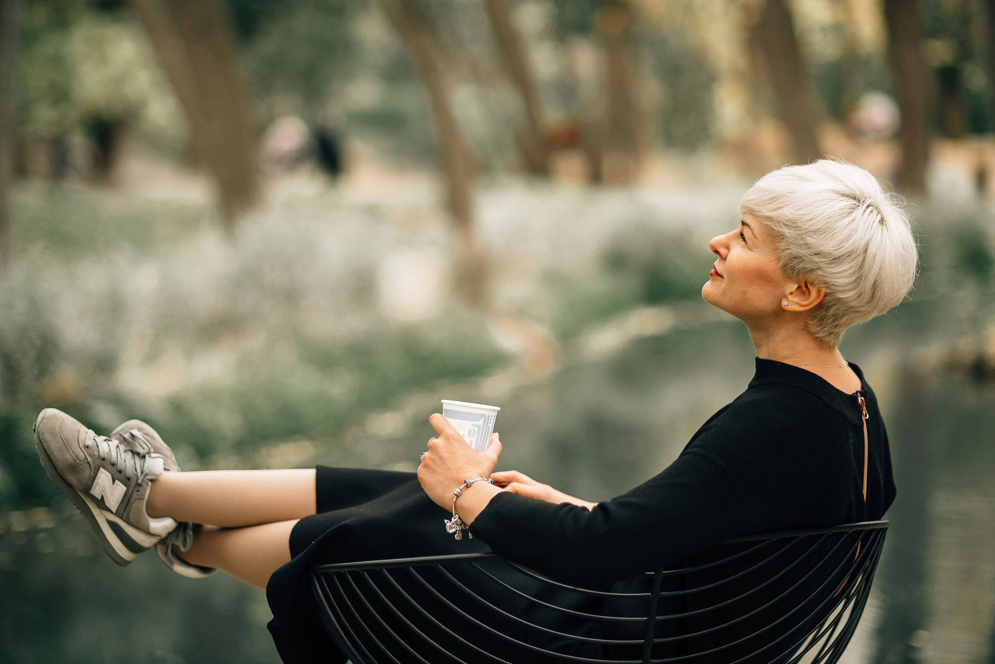 A woman resting outdoors with a warm drink between appointments